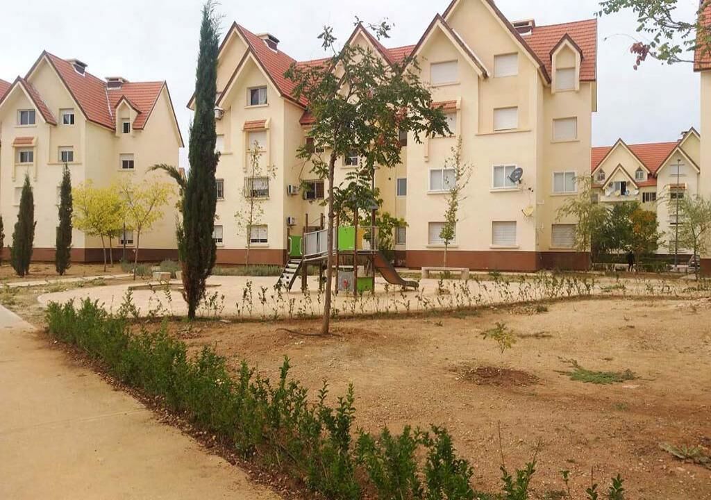 Un immeuble résidentiel doté de nombreux balcons, d’une aire de jeux et d’un espace paysager agrémenté d’arbres et d’arbustes.