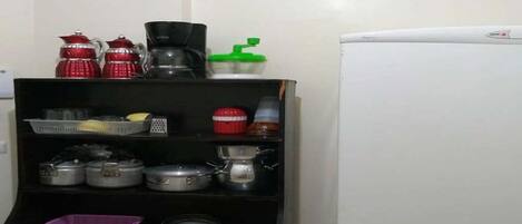 Una cocina con refrigerador, estantes con ollas, cafetera y tetera.
