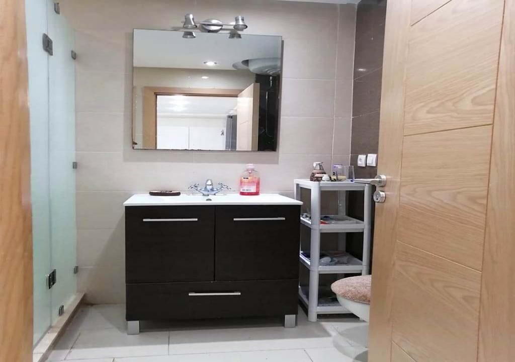 Een moderne badkamer met een donkere wastafel, een spiegel en een plank.