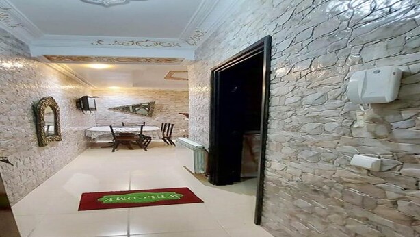 Un hall de hotel con pared de piedra, un comedor con mesa y sillas, y una alfombra roja que conduce a la entrada.