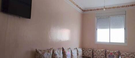 A room with a sofa, a television mounted on the wall, and a window with blinds.