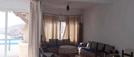 A spacious living room with a sofa set, a round table, and a view of a mountainous landscape through large windows.