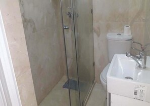 Ein Badezimmer mit Duschkabine aus Glas, einem weißen Waschbecken und einer Toilette.