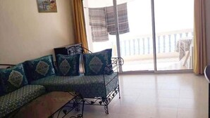 A living room with a curved sofa, a small table, and a balcony with a view. - Pleasant Sea Front Apartment in Taghazout 4966 (Taghazout)