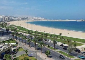 A coastal road with palm trees, a beach, and a cityscape in the background. - Beautiful apartment in Tangier 4969 (Tanger)