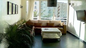 A living room with a sofa, a coffee table, and a large window with a view of buildings. - Superb sea view apartment in Fakhama 4970 (Tanger)