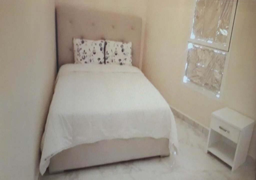 A bedroom with a bed, a nightstand, and a window.