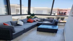 A modern living area with a sectional sofa and a small coffee table, large windows offering a view of the cityscape.