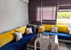 A room with a blue sofa set, yellow cushions, a white chair, and a table with a glass. - Pleasant apartment in La Perla Saidia 4974 (Saidia)