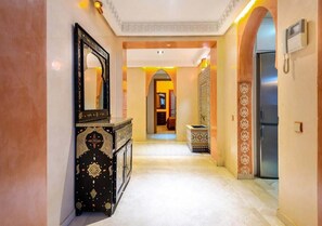 Un pasillo con suelo de mármol, una consola negra con detalles decorativos, un espejo y una puerta con un diseño en la pared.