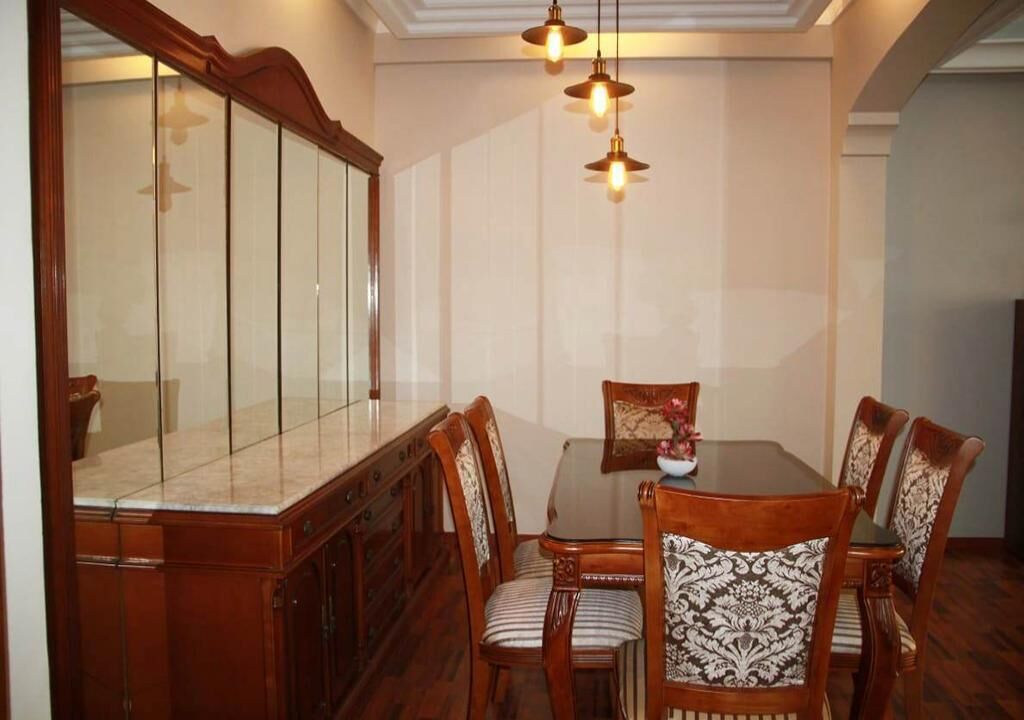Uma sala de jantar com uma mesa de madeira, seis cadeiras e um espelho grande.