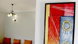 Een kamer met een houten eettafel, een kroonluchter en een kleurrijk abstract schilderij aan de muur.