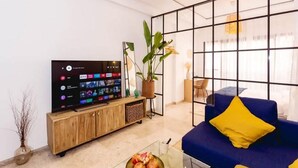 A modern living room with a flat-screen TV, a blue sofa with yellow cushions, a wooden cabinet, and a large window with a grid pattern. - Residence La Perle de Marrakech 4990 (Marrakech)