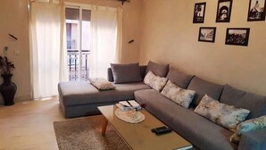 Una sala de estar con un sofá gris, una mesa de centro y un balcón con cortinas.