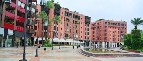 A public square with a fountain, surrounded by multi-story buildings with balconies and shops.