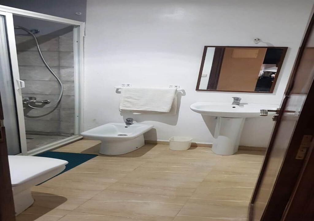 Een badkamer met douche, toilet, bidet, wastafel en spiegel.