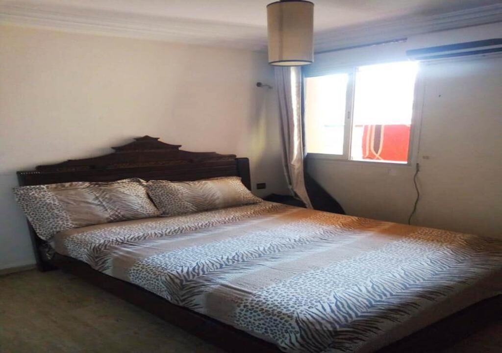 A bedroom with a bed, a nightstand, a lamp, and a window with curtains.