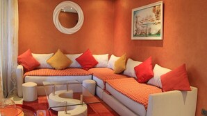 Una sala de estar moderna con un sofá seccional, una mesa de centro de vidrio y un espejo redondo en la pared.