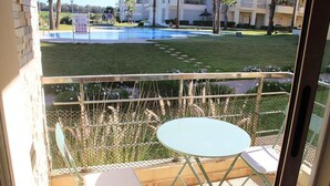 Un balcón con mesa y sillas, una piscina al fondo y una zona con césped.