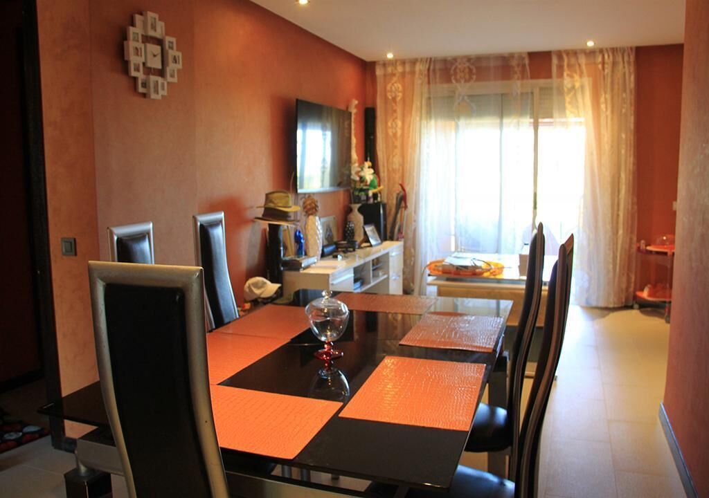 Un comedor con una mesa negra y manteles individuales anaranjados, rodeado de sillas.