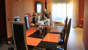 Un comedor con una mesa negra y manteles individuales anaranjados, rodeado de sillas.