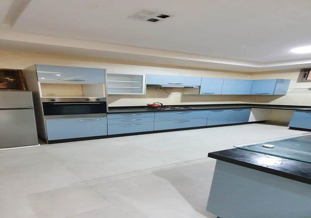 A modern kitchen with light blue cabinets, a stainless steel refrigerator, and a black countertop.