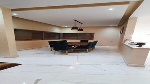 Een ruime eetruimte met een marmeren vloer, een houten tafel en groene fauteuils.