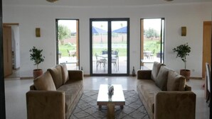 A spacious living room with two sofas facing a large sliding glass door leading to an outdoor patio. There are two potted plants, a coffee table, and two hanging light fixtures. - Pleasant villa with swimming pool in Marrakech 5100 (Marrakech)