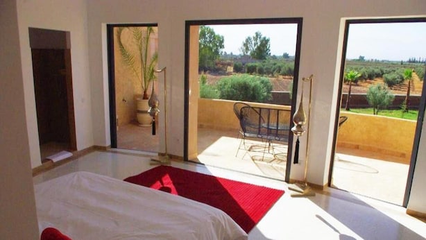 A bedroom with a bed, a red rug, and a view of an outdoor patio with a chair and a plant. - Pleasant villa with swimming pool in Marrakech 5100 (Marrakech)