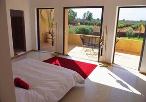 A bedroom with a bed, a red rug, and a view of an outdoor patio with a chair and a plant. - Pleasant villa with swimming pool in Marrakech 5100 (Marrakech)