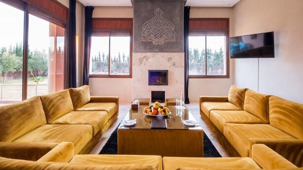 Ein Zimmer mit zwei gelben Sofas, die einem zentralen Tisch mit Obstschale, Kamin und Fernseher an der Wand zugewandt sind.