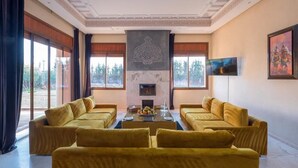 Ein geräumiges Wohnzimmer mit Kamin, großen Fenstern und einem Fernseher.