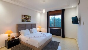 Ein Schlafzimmer mit Bett, Nachttischen, einem Gemälde, einem Fenster und einem an der Wand montierten Fernseher.