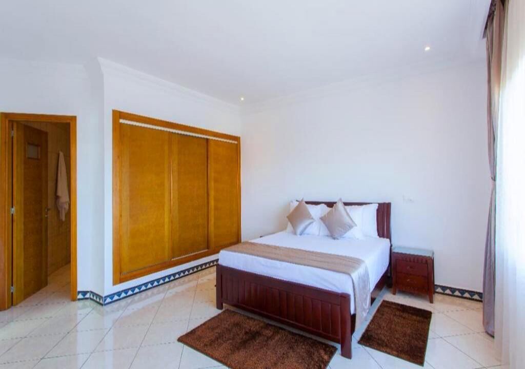 A bedroom with a large bed, a wardrobe, and a small bedside table.