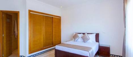 A bedroom with a large bed, a wardrobe, and a small bedside table.