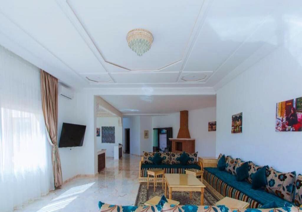 A spacious living room with a sofa set, a coffee table, and a television mounted on the wall.