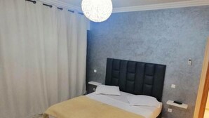 Une chambre à coucher avec un lit, des rideaux blancs, un mur gris à texture et un luminaire suspendu.