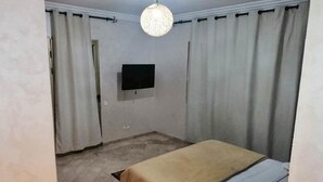 Une chambre à coucher avec un lit, des rideaux, un téléviseur et un luminaire suspendu.