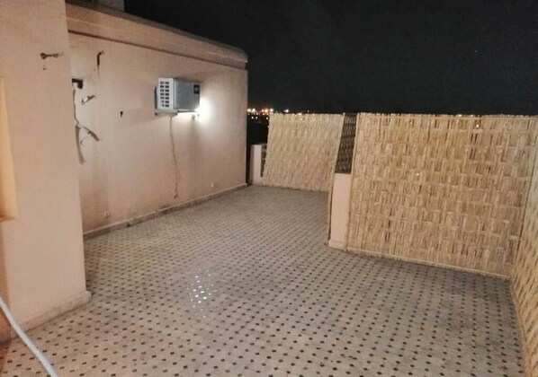 A rooftop terrace with a perforated floor, a wall-mounted air conditioning unit, and a woven wall.