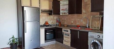 Een koelkast, een oven, een kookplaat, kookgerei, borden en bestek