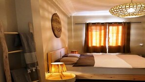 A bedroom with a bed, a bedside table with a lamp, a hanging light fixture, and a window with curtains.
