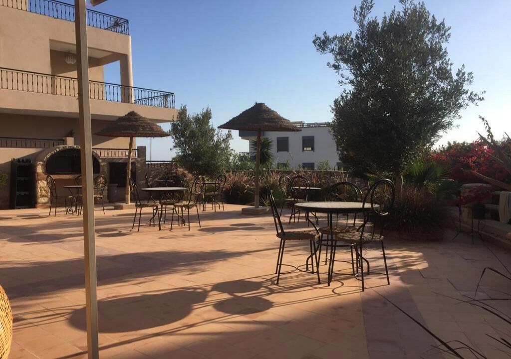 An outdoor patio area with tables and chairs, a building with balconies, and a tree.