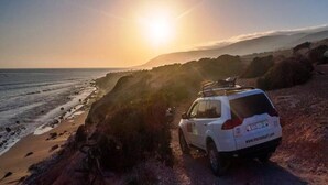 Ein weißer SUV parkt am Strand, im Hintergrund ein sonniger Himmel.