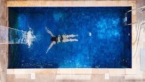 Ein rechteckiger Swimmingpool mit einer schwimmenden Person, umgeben von gefliesten Wänden.