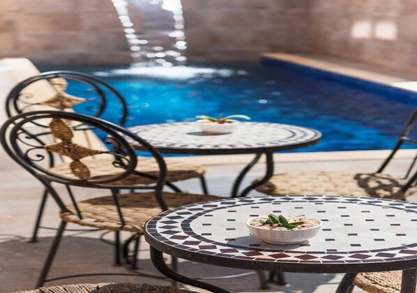 A poolside area with a mosaic table, wicker chairs, and a small bowl of snacks.