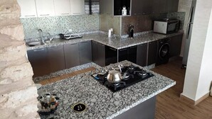 Cocina compacta con encimeras de granito, estufa a gas, microondas y lavadora.