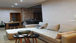 Una sala de estar moderna con un sofá modular, un comedor y una cocina visible a través de un arco abierto.
