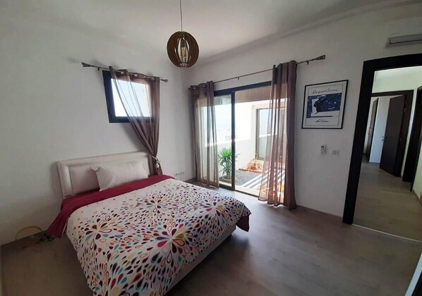 A bedroom with a bed, a window with curtains, a door, and a hallway.
