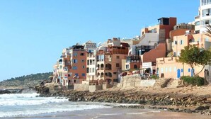 A coastal building with multiple balconies, a sandy beach, and a rocky shoreline. - Superb villa in Taghazout bay 5197 (Taghazout)