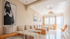 A spacious living room with a sectional sofa, a round coffee table, and a large window providing natural light. - Moroccan Surf Adventures 5223 (Imi Ouaddar)